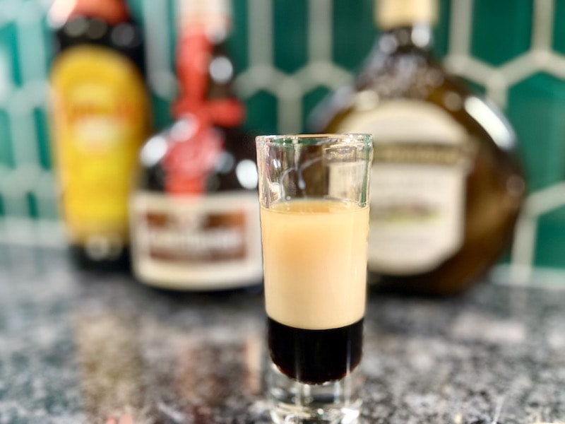 Coffee cocktails B-52 shooter on counter in front of kahlua, grand marnier, irish cream bottles
