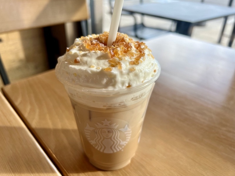 Starbucks iced caramel brulee latte on cafe table with paper straw