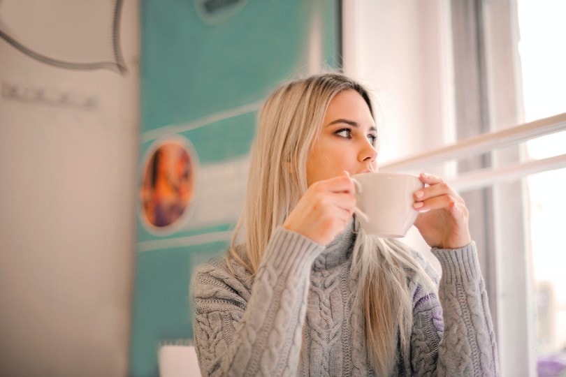 a woman in grey holding a white cup