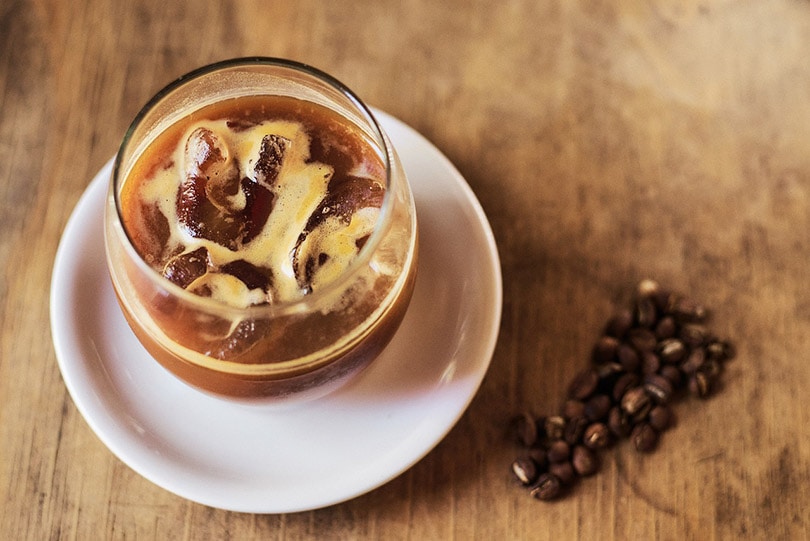 a glass of iced coffee on a white saucer