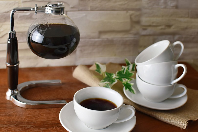 siphon coffee maker on wooden table near coffee cups