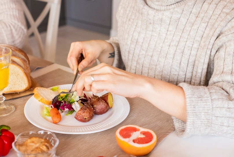 a cropped woman in a sweater eating vegetables