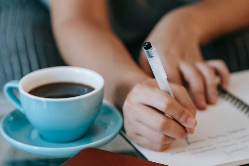 student writing on her notebook near a cup of coffee