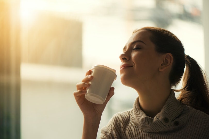 woman closing her eyes and smiling with a coffee cup in her hand