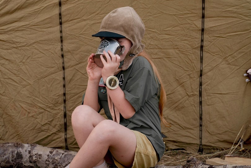 a girl sitting on tree trunk drinking from stainless steel mug