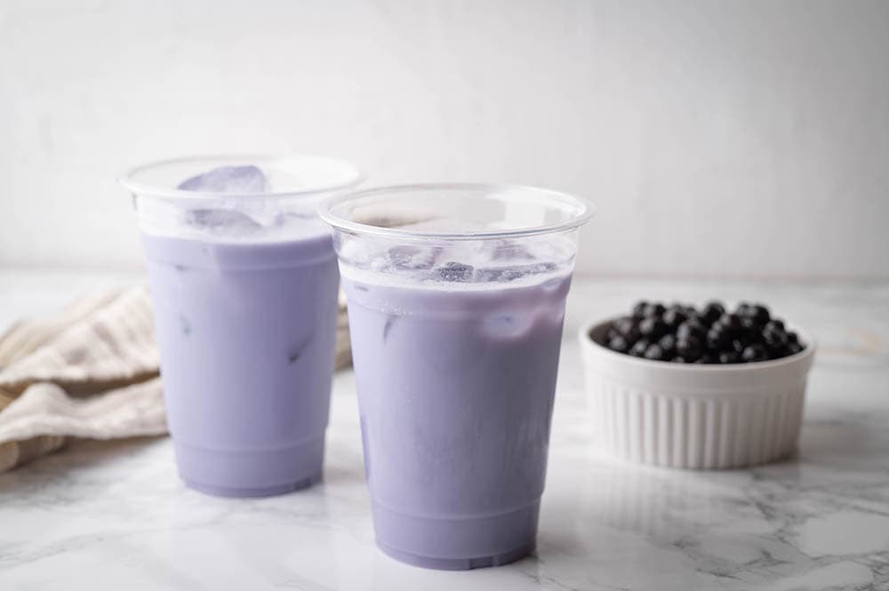 two cups of iced taro milk tea with a bowl of boba on the side
