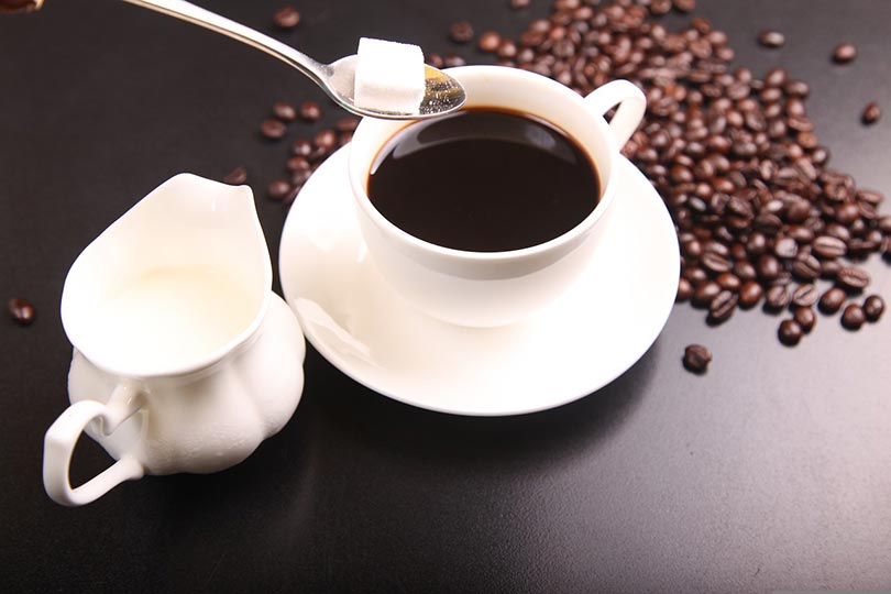 adding sugar into a cup of coffee