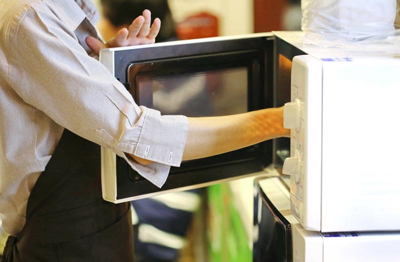 a woman picking up something from the microwave
