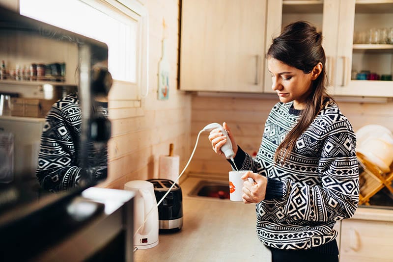 Woman frothing milk using immersion blender