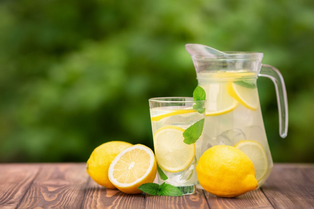 lemonade in glass and jug on wooden table outdoors. Summer refreshing drink. Cold detox water with lemon