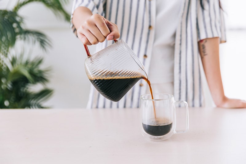 barista hand pouring freshly brewed drip coffee in a glass mug